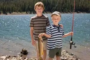 2 young boys, brothers at lake shore holding up the latest catch