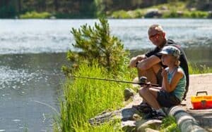 father and son sitting on rocky bank son fishing with rod and reel